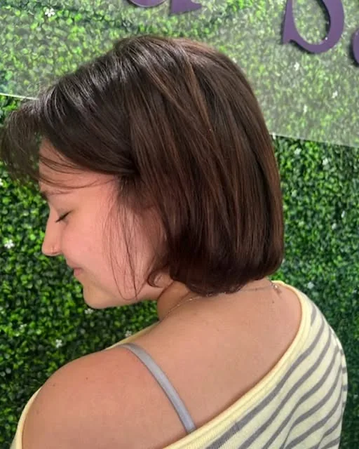 Chin-length brunette bob haircut in front of the LuLu green wall