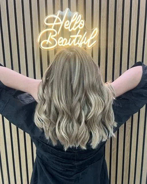 Blonde balayage with soft waves under the Hello Beautiful sign